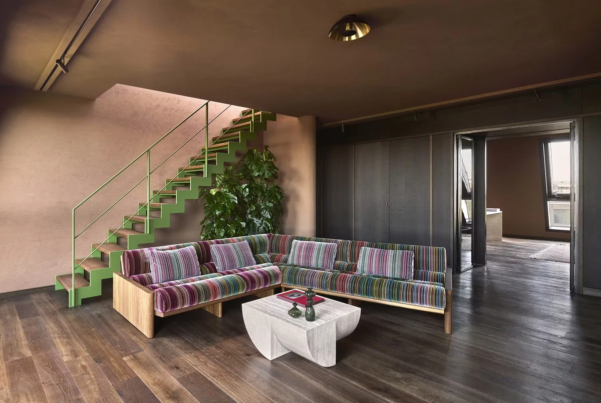 Salon aux murs en enduit terre crue rosé, escalier vert et banquettes colorées, ambiance chaleureuse