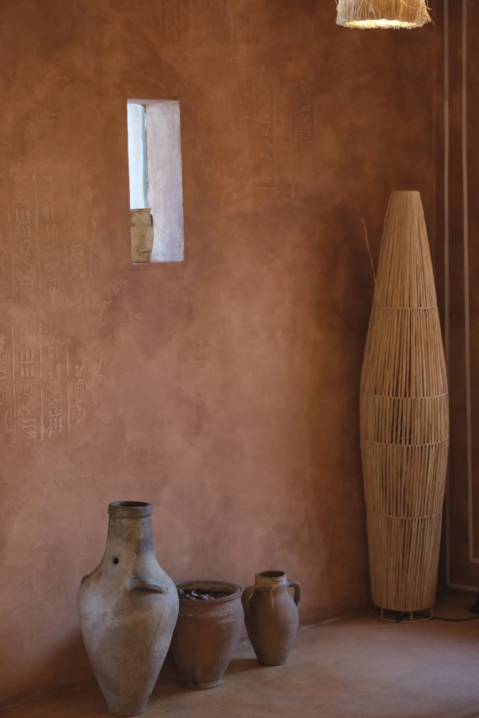 Mur en enduit Chukum teinte terracotta, niche murale et jarres en terre cuite dans un intérieur méditerranéen